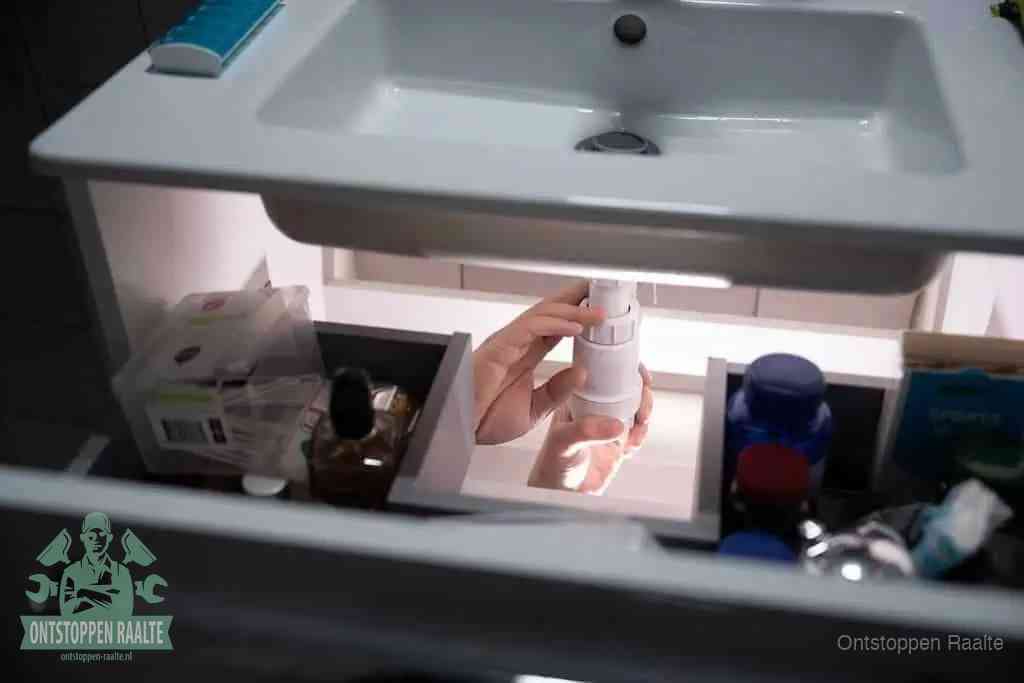 Een pompfles met zeep boven een wastafel, de heet water en afwasmiddel-methode om een vetprop in de afvoer los te maken in Raalte