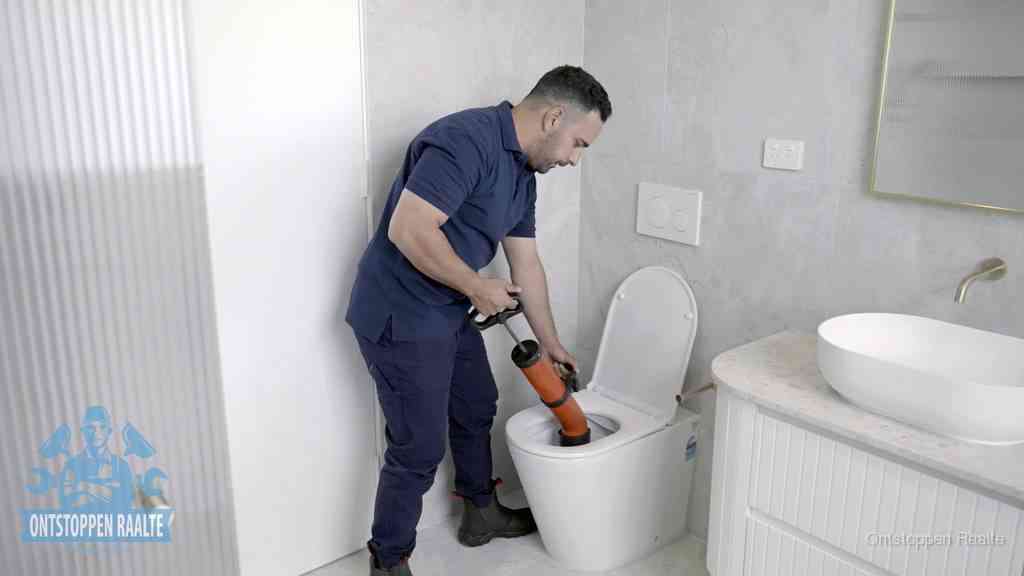 Een monteur buigt over een wandcloset en duwt met de hand een persluchtontstopper in de toiletpot om de verstopping handmatig los te maken in Raalte