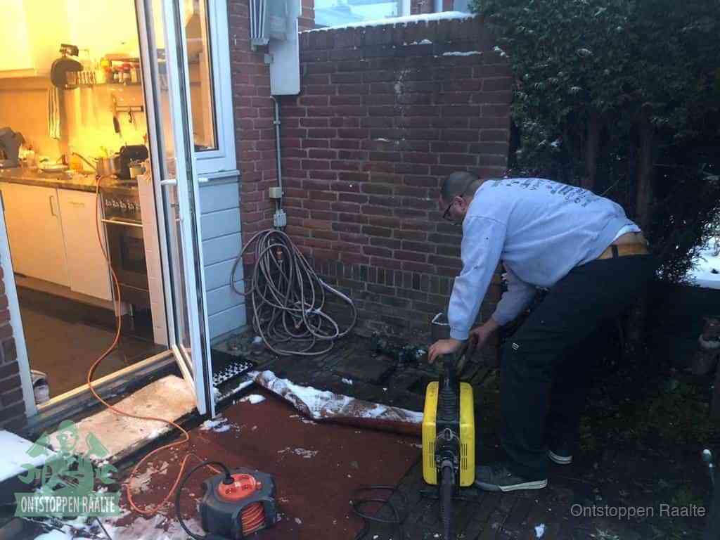 Een monteur werkt buiten bij een open riool-/grondput met een elektrische ontstoppingsmachine om een verborgen afvoerprobleem op te sporen in Raalte