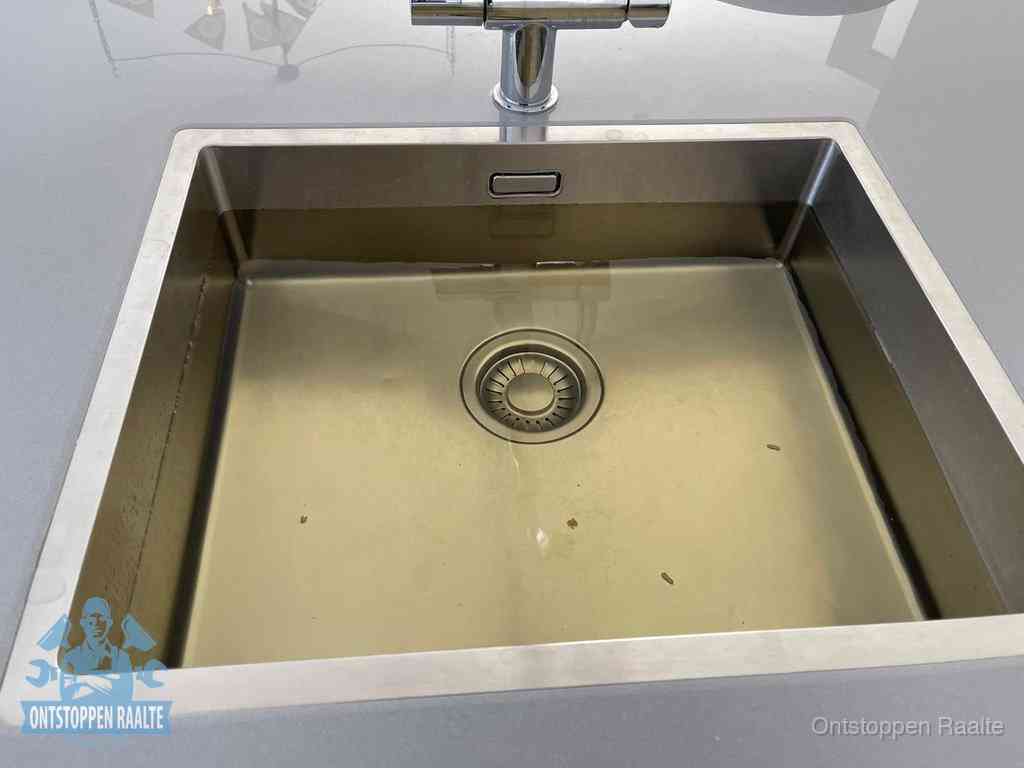 Stilstaand water in een rvs spoelbak dat niet wegloopt, een duidelijk signaal van een gootsteenverstopping in Raalte