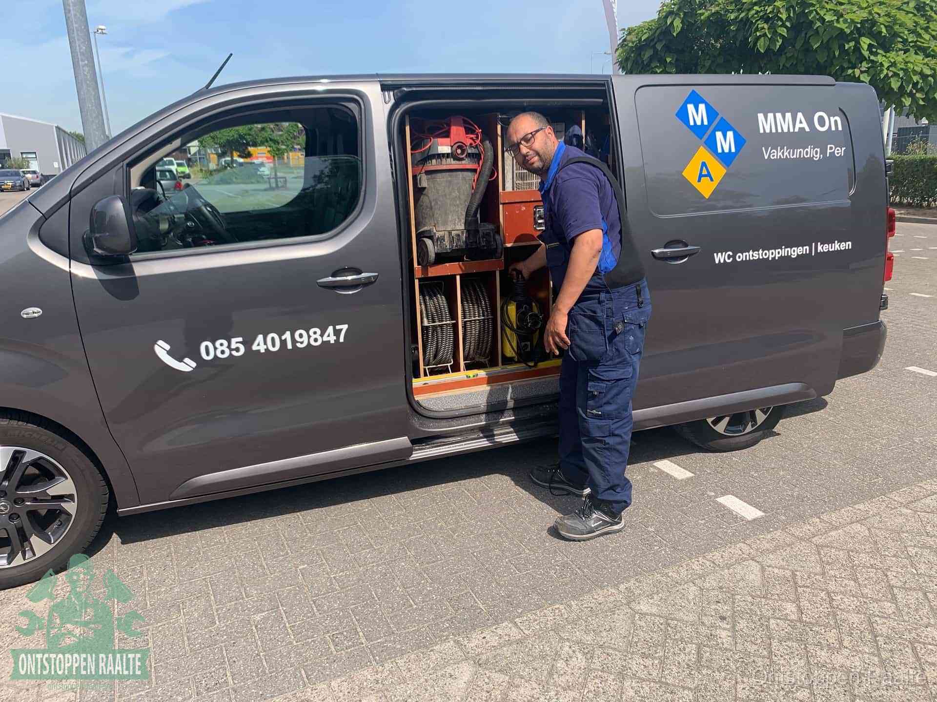 Een monteur bij de open schuifdeur van zijn bedrijfsbus op een parkeerplaats, klaar om de oorzaak van terugkerende afvoerverstoppingen aan te pakken in Raalte