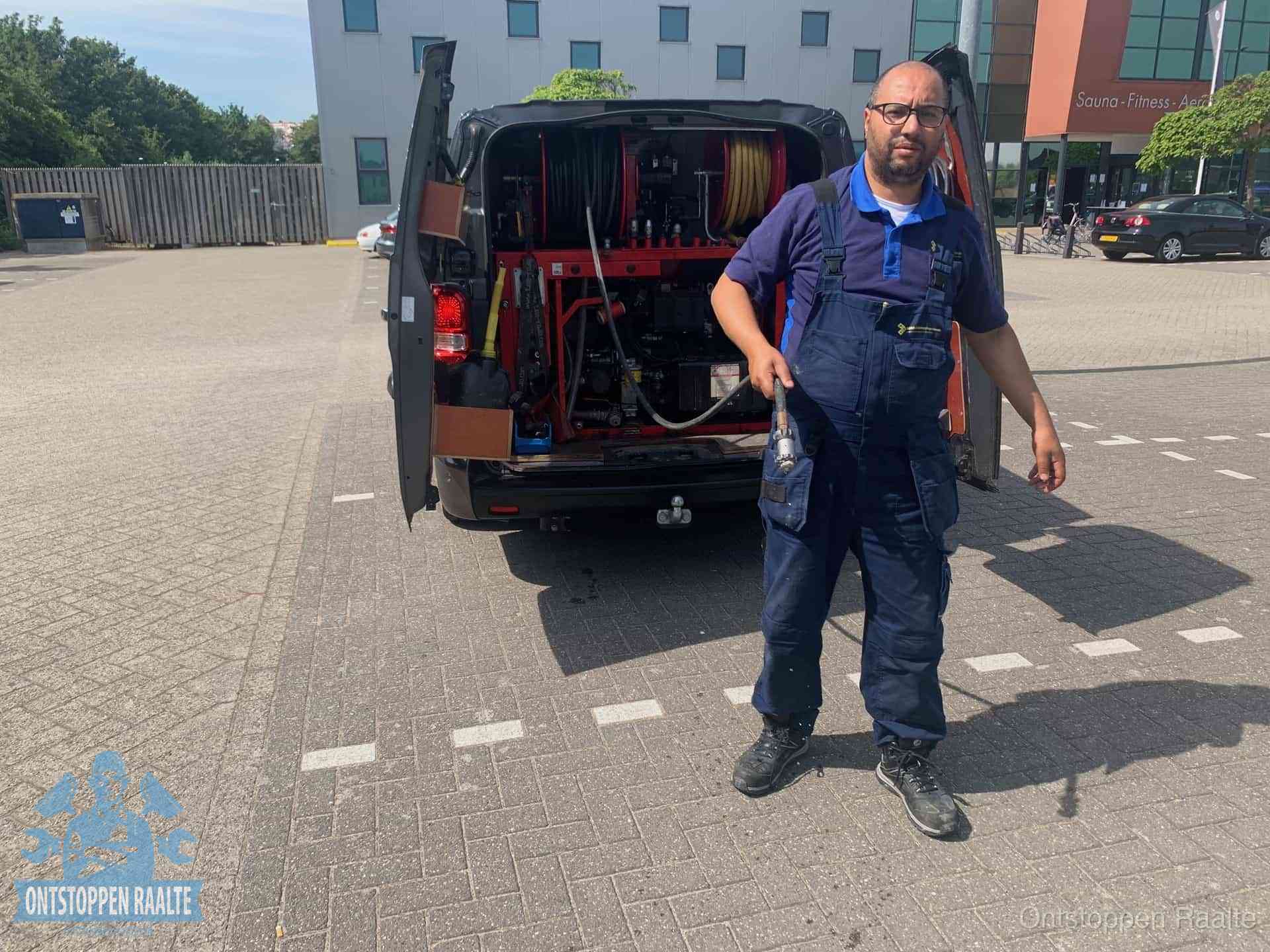 Een monteur bij zijn bestelbus met een hogedruk- en rioolreinigingsunit, klaar om de oorzaak van terugkerende wc-verstoppingen aan te pakken in Raalte