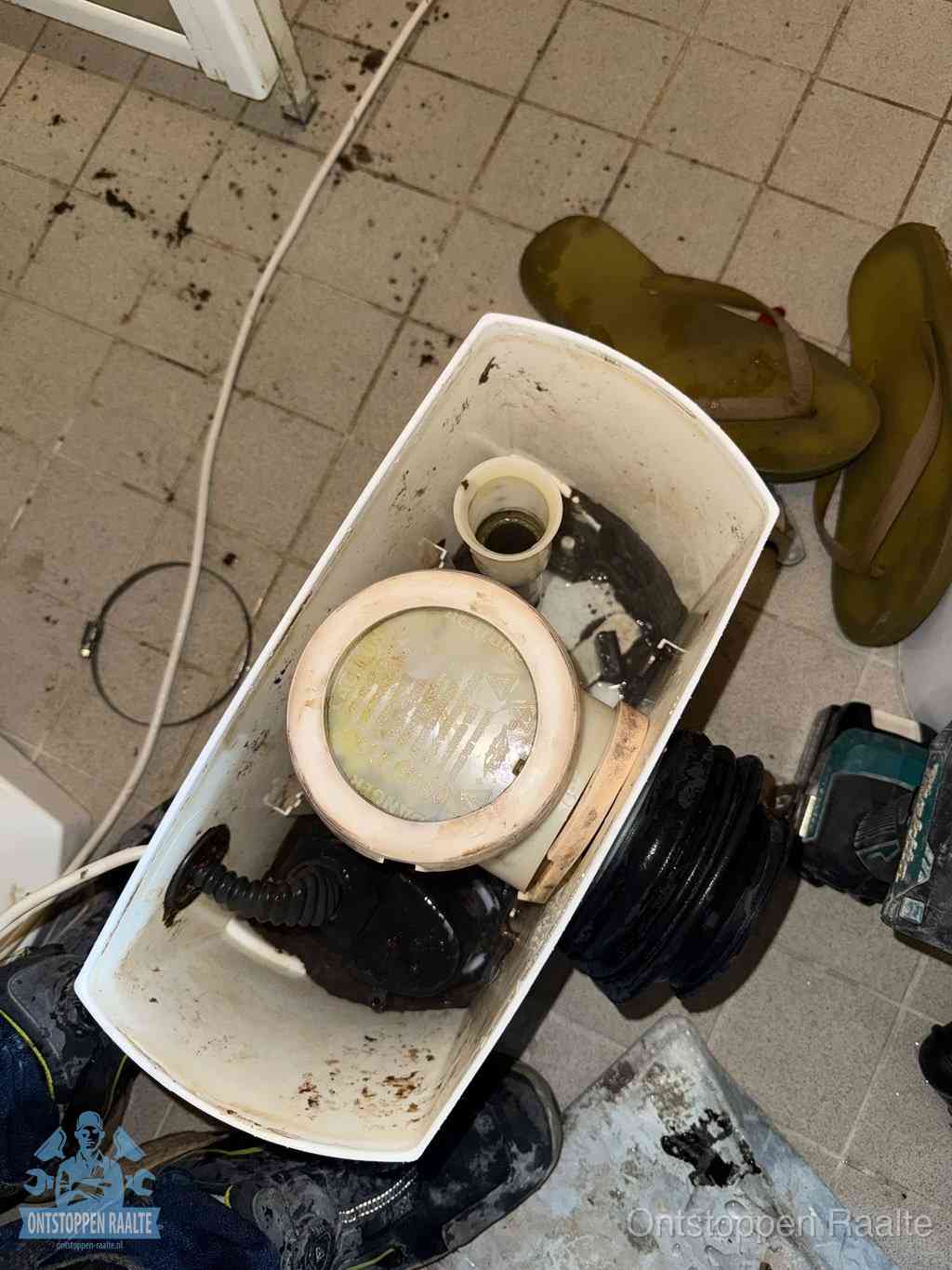 Een gedemonteerde toiletpot op de vloer met ontstoppingsveer en gereedschap ernaast, het verwijderen van een vastzittend voorwerp uit de wc in Raalte