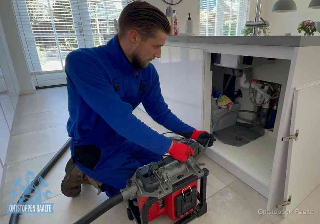 Een monteur voert een professionele elektrische ontstoppingsmachine in de afvoer onder de spoelbak tijdens het gootsteen ontstoppen in Raalte