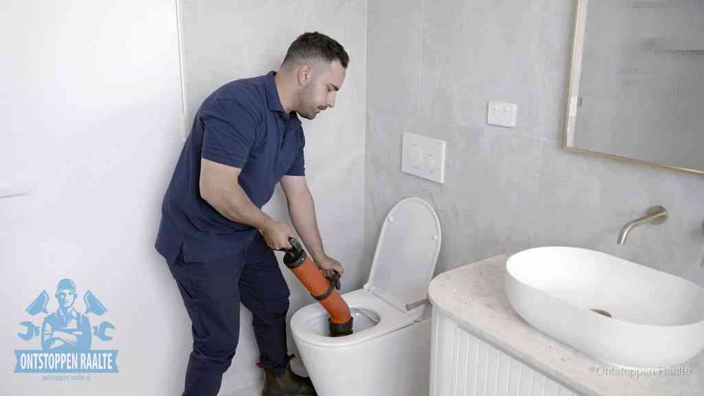 Een man gebruikt een handmatige luchtdruk-ontstopper in een modern betegeld toilet om zelf de wc te ontstoppen in Raalte